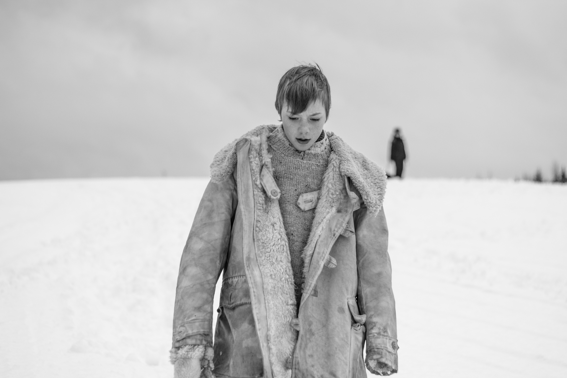 Young actor walking through snow with a figure in the distance