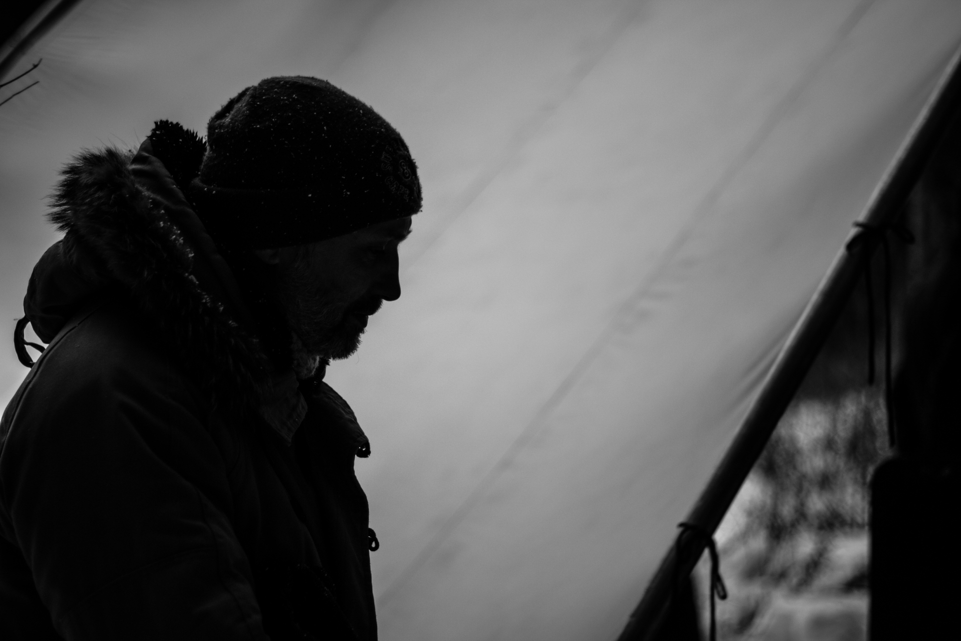 Silhouette portrait of a bearded man in a winter parka beside a tent